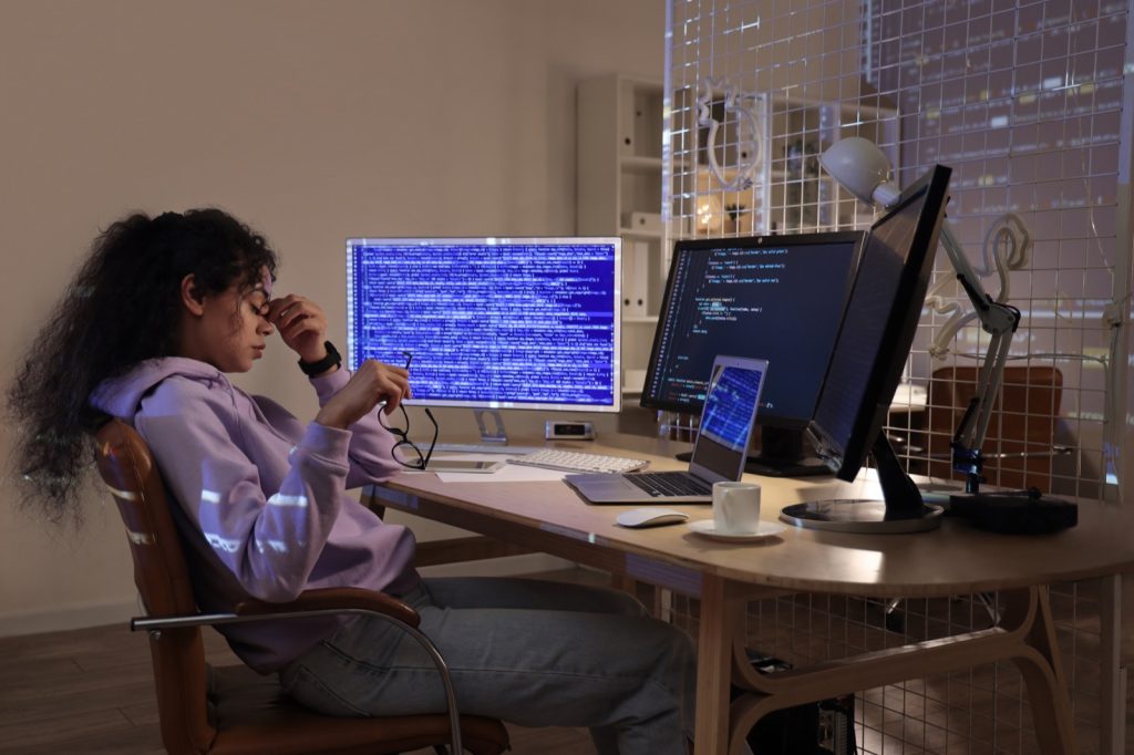 Vermoeide developer wrijft 's avonds in haar ogen achter meerdere schermen met code